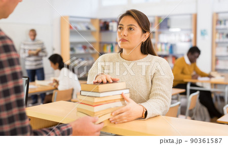 Young Latina returning books to librarian in public library Young Latina returning books to librarian in public library 90361587