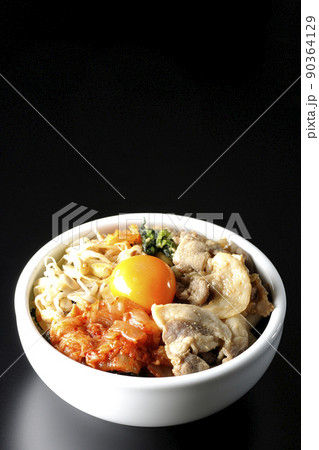 もやしナムルやキムチ、豚肉など沢山の具材が入っているビビンバ丼を黒背景で撮影 90364129