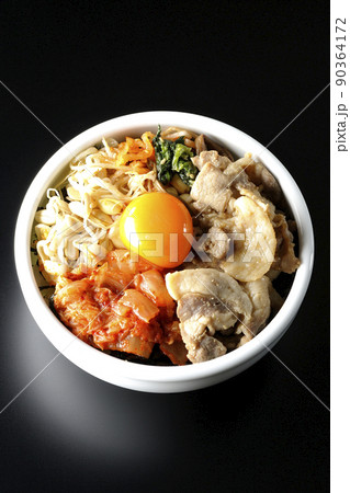 もやしナムルやキムチ、豚肉など沢山の具材が入っているビビンバ丼を黒背景で俯瞰撮影 90364172
