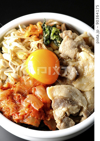 もやしナムルやキムチ、豚肉など沢山の具材が入っているビビンバ丼を黒背景で俯瞰撮影 90364175