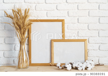 Vase with ears of wheat and photo frames against brick wall Vase with ears of wheat and photo frames against brick wall 90369391