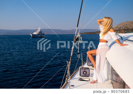 Beautiful young blond woman in a dress standing on yacht stern on the sea or ocean Beautiful young blond woman in a dress standing on yacht stern on the sea or ocean 90370685