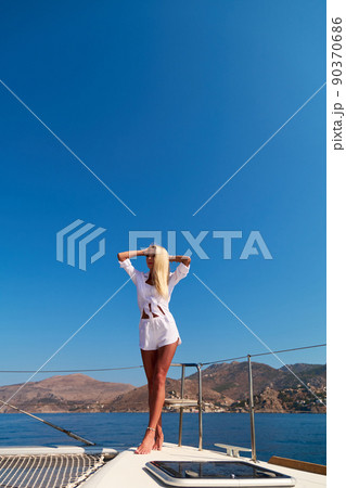 Beautiful young blond woman in bikini standing on catamaran at sunny summer day 90370686