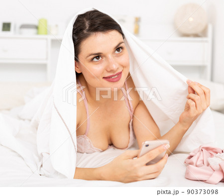 Sexy woman relaxing under blanket and looking at smartphone Sexy woman relaxing under blanket and looking at smartphone 90373098