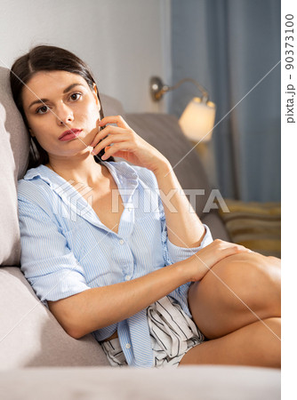Sad girl sitting on sofa in living room Sad girl sitting on sofa in living room 90373100