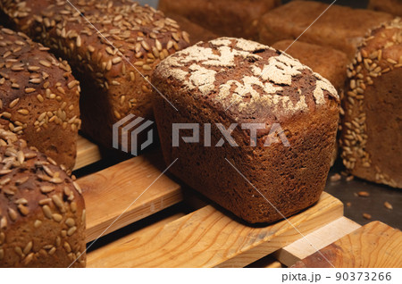 Close-up rye loaves of hot rye bread stand on a wooden tray in a dark bakery room 90373266