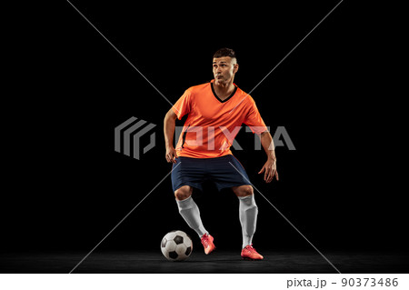 Dynamic portrait of professional male football soccer player in motion isolated on dark background. Concept of sport, goals, competition, hobby, achievements 90373486