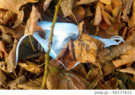 Used medical mask in yellow leaves. The spread of the coronavirus. Protection against Covid-19. The onset of another wave of the virus. 90375833