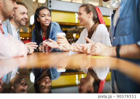 Group of cheerful young multi-ethnic friends sitting at table on food court and discussing last news Group of cheerful young multi-ethnic friends sitting at table on food court and discussing last news 90376551