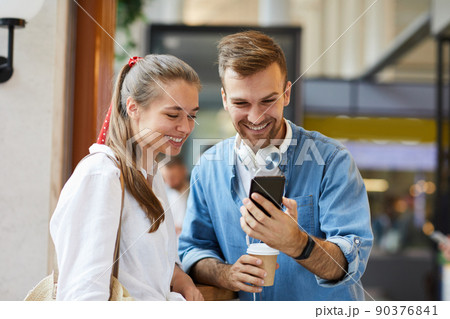 Cheerful young friends in casual clothing standing in cafe and watching online video on smartphone 90376841