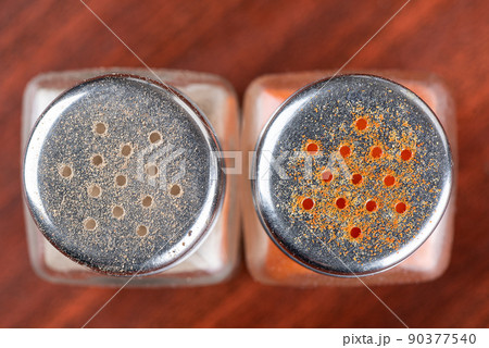 Top view of the lids of two glass pepper pots with black and red ground peppers. 90377540
