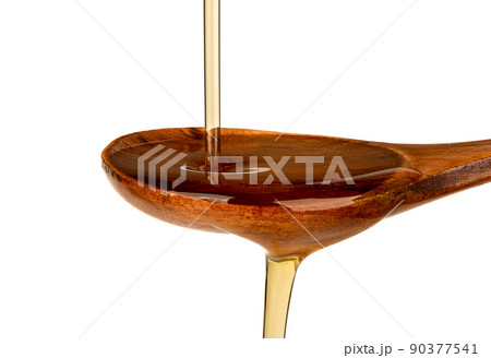 Close-up of a jet of sunflower oil and a wooden spoon on a white background. 90377541