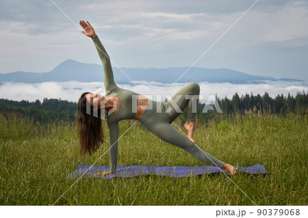 Fitness caucasian woman dressed in sport clothes practising yoga among green mountains. Outdoors activity during leisure time.  90379068