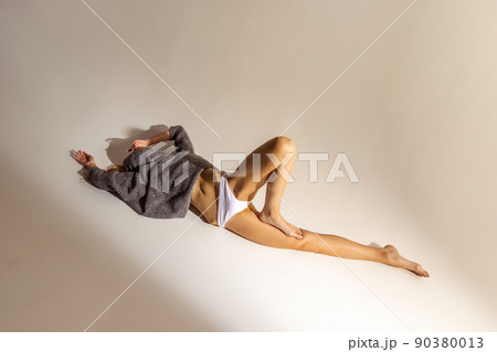 Full-length portrait of young slim woman in oversized sweater and underwear posing isolated over grey studio background. Textured body Full-length portrait of young slim woman in oversized sweater and underwear posing isolated over grey studio background. Textured body 90380013