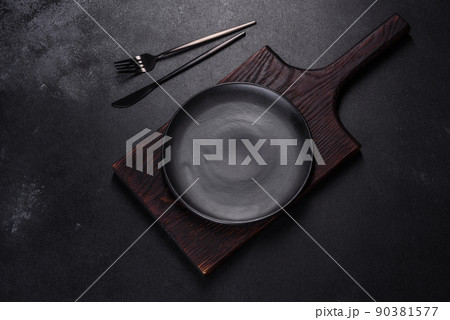 An empty plate with a knife, fork or spoon with a wooden cutting board An empty plate with a knife, fork or spoon with a wooden cutting board 90381577
