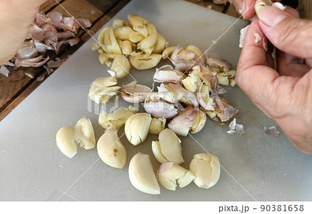Woman peeling garlic on the cutting board for cooking Woman peeling garlic on the cutting board for cooking 90381658