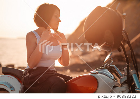 Silhouette of beautiful adult woman standing near motorcycle with helmet. Sunset on the background. Concept of motorcycle travel and feminism 90383222