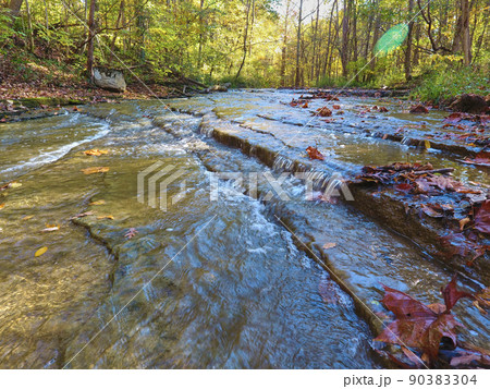 Small waterfall over flat slates of rock with fall leaves 90383304
