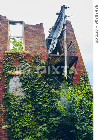 Vertical of abandoned red brick building falling apart and covered in vines Vertical of abandoned red brick building falling apart and covered in vines 90383486