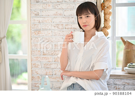 キッチンでマグカップで飲み物を飲む若い女性 キッチンでマグカップで飲み物を飲む若い女性 90388104