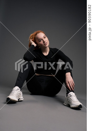 Smiling redhead young sportswoman resting on floor in studio 90390182