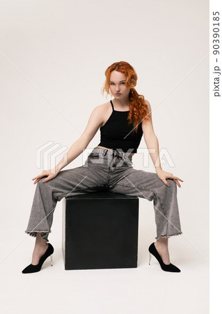 Confident young lady sitting on cube and looking at camera 90390185