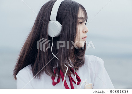 海辺で音楽を聞くセーラー服を着た女子高生 90391353