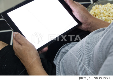 Glass cup with salted popcorn & digital tablet in a gray armchair. Glass cup with salted popcorn & digital tablet in a gray armchair. 90391951