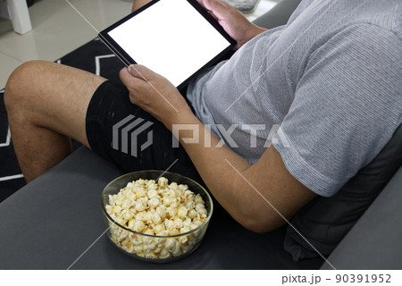 Glass cup with salted popcorn & digital tablet in a gray armchair. Glass cup with salted popcorn & digital tablet in a gray armchair. 90391952