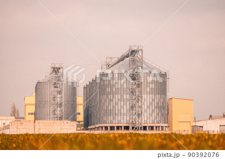 Grain elevator. Metal grain elevator in agricultural zone. Agriculture storage for harvest. Grain elevators on green nature background. Exterior of agricultural factory. Nobody. 90392076
