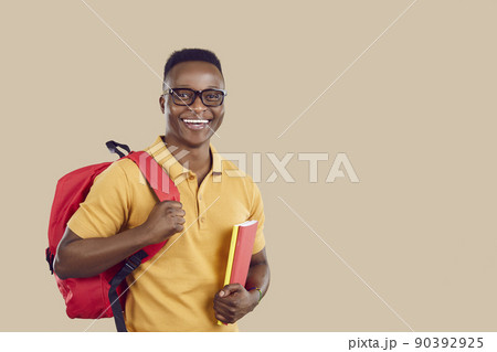 Happy African American student with bag and books standing on beige copy space background 90392925