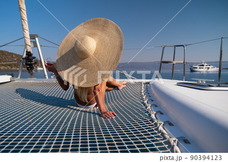 Beautiful young blond woman in bikini sitting on catamaran bow at sunny summer day 90394123