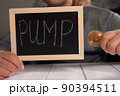Close-up of a woman holding a board with the inscription PUMP and a gold bitcoin 90394511