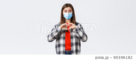 Different emotions, covid-19 pandemic, coronavirus self-quarantine and social distancing concept. Excited young woman in medical mask making confession, show heart sign like someone, express sympathy Different emotions, covid-19 pandemic, coronavirus self-quarantine and social distancing concept. Excited young woman in medical mask making confession, show heart sign like someone, express sympathy 90396182