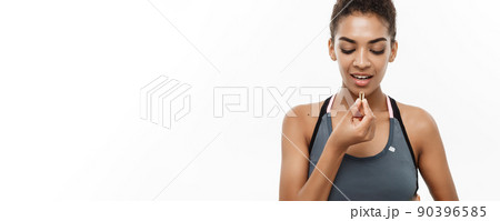 Healthy and Fitness concept - Closeup portrait of beautiful African American taking a pill of Cod liver oil. Isolated on white studio background. 90396585