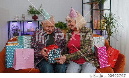 Happy old senior family grandparents man woman celebrating birthday anniversary on couch at home Happy old senior family grandparents man woman celebrating birthday anniversary on couch at home 90402767