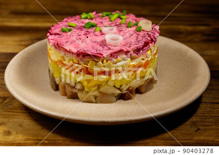 Traditional russian salad "Herring under a fur coat" (shuba) on wooden table. Layered salad with herring, beets, carrots, onions, potatoes and eggs 90403278