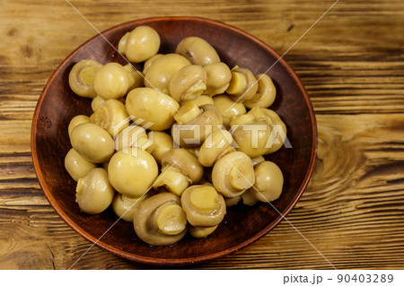 Ceramic plate with pickled champignons. Marinated mushrooms on wooden table 90403289