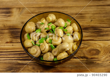 Glass bowl with pickled champignons. Marinated mushrooms on wooden table 90403290