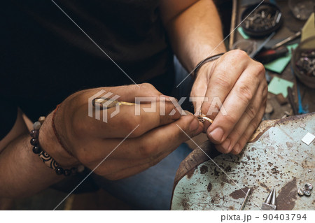 A jeweler is taking apart a gold ring with stones in a workshop, close-up 90403794