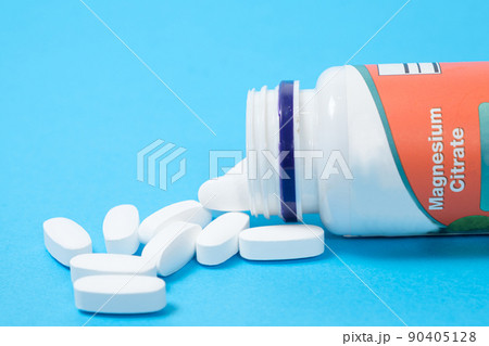 Magnesium citrate pills spill out of a jar on a blue background. Magnesium citrate pills spill out of a jar on a blue background. 90405128