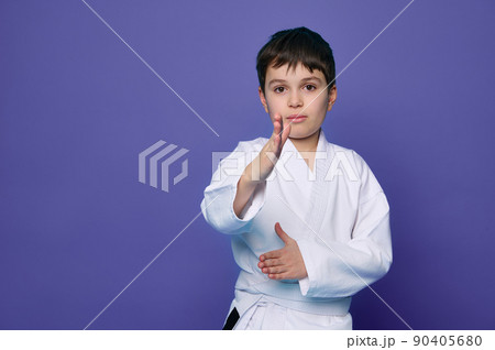 Martial arts attack. School age boy aikido fighter in white kimono isolated over purple background with copy space for advertising text. 90405680