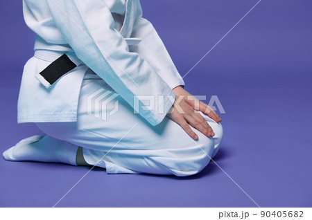 Cropped view of child aikido wrestler in white kimono sitting in stance with hands on knees isolated on purple background with copy space. Concept of Oriental Martial Arts practice 90405682