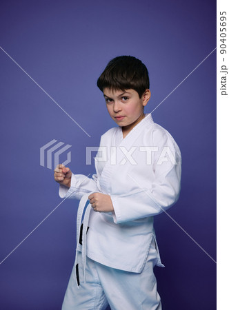 Portrait of a handsome Caucasian teenage boy, aikido wrestler practicing martial skills against purple wall background. Oriental martial arts concept Portrait of a handsome Caucasian teenage boy, aikido wrestler practicing martial skills against purple wall background. Oriental martial arts concept 90405695
