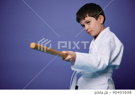 Waist length portrait of a confident teenage boy in white kimono practices wooden bokken in Aikido training on purple background with copy ad space 90405698