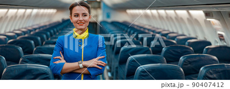 Joyful woman stewardess standing in aircraft passenger cabin 90407412