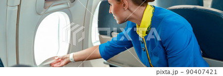 Female flight attendant opening window in airplane 90407421