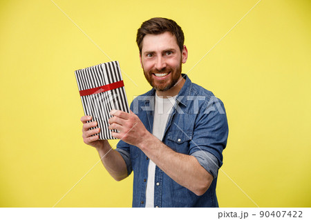 Handsome smiling man shaking gift box and looking at camera. Great present 90407422