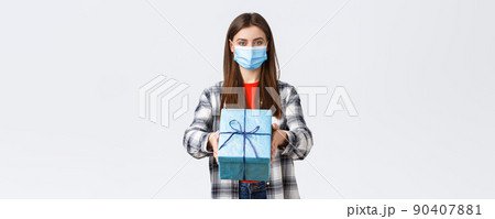 Covid-19, lifestyle, holidays and celebration concept. Cheerful young girl in medical mask stretch hand, handing birthday gift to you, smiling, congratulate with b-day, white background Covid-19, lifestyle, holidays and celebration concept. Cheerful young girl in medical mask stretch hand, handing birthday gift to you, smiling, congratulate with b-day, white background 90407881