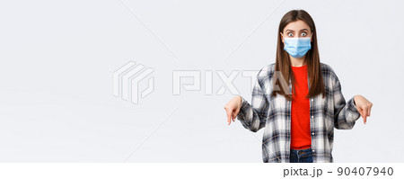 Coronavirus outbreak, leisure on quarantine, social distancing and emotions concept. Shocked and impressed young woman in medical mask and casual outfit, pointing fingers down, stare camera Coronavirus outbreak, leisure on quarantine, social distancing and emotions concept. Shocked and impressed young woman in medical mask and casual outfit, pointing fingers down, stare camera 90407940
